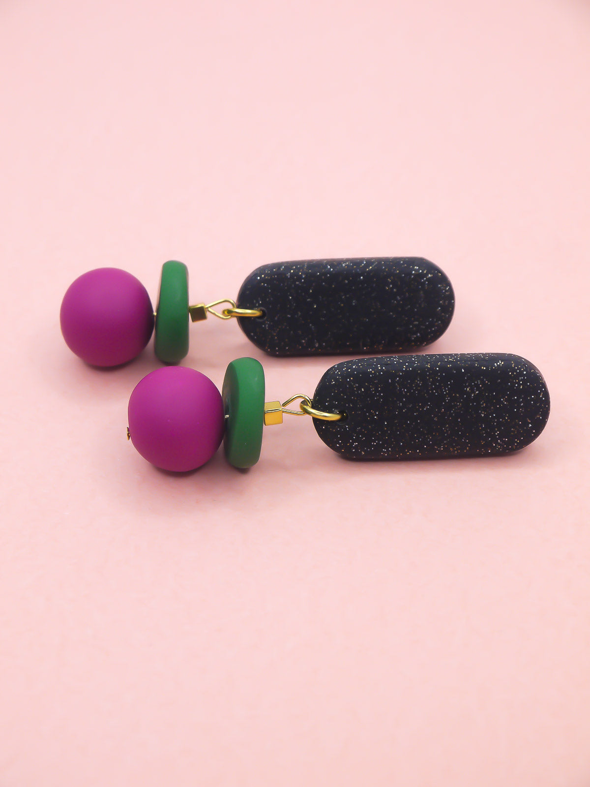 Pair of earrings with colorful spherical beads on a pink background