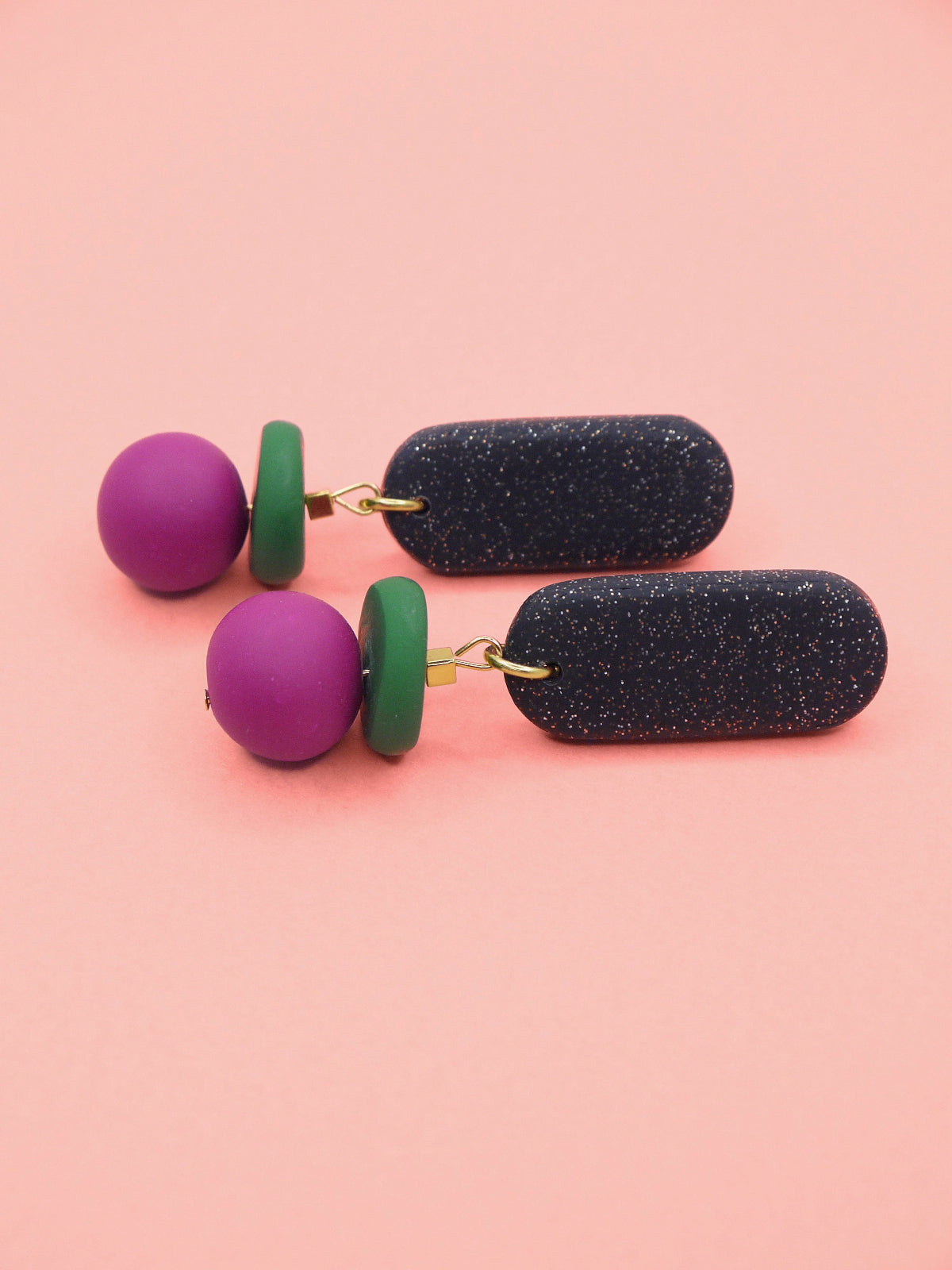 Pair of earrings with black, green, and pink beads on a pink background