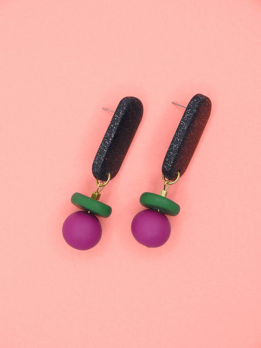 Pair of earrings with black, green, and pink beads on a pink background