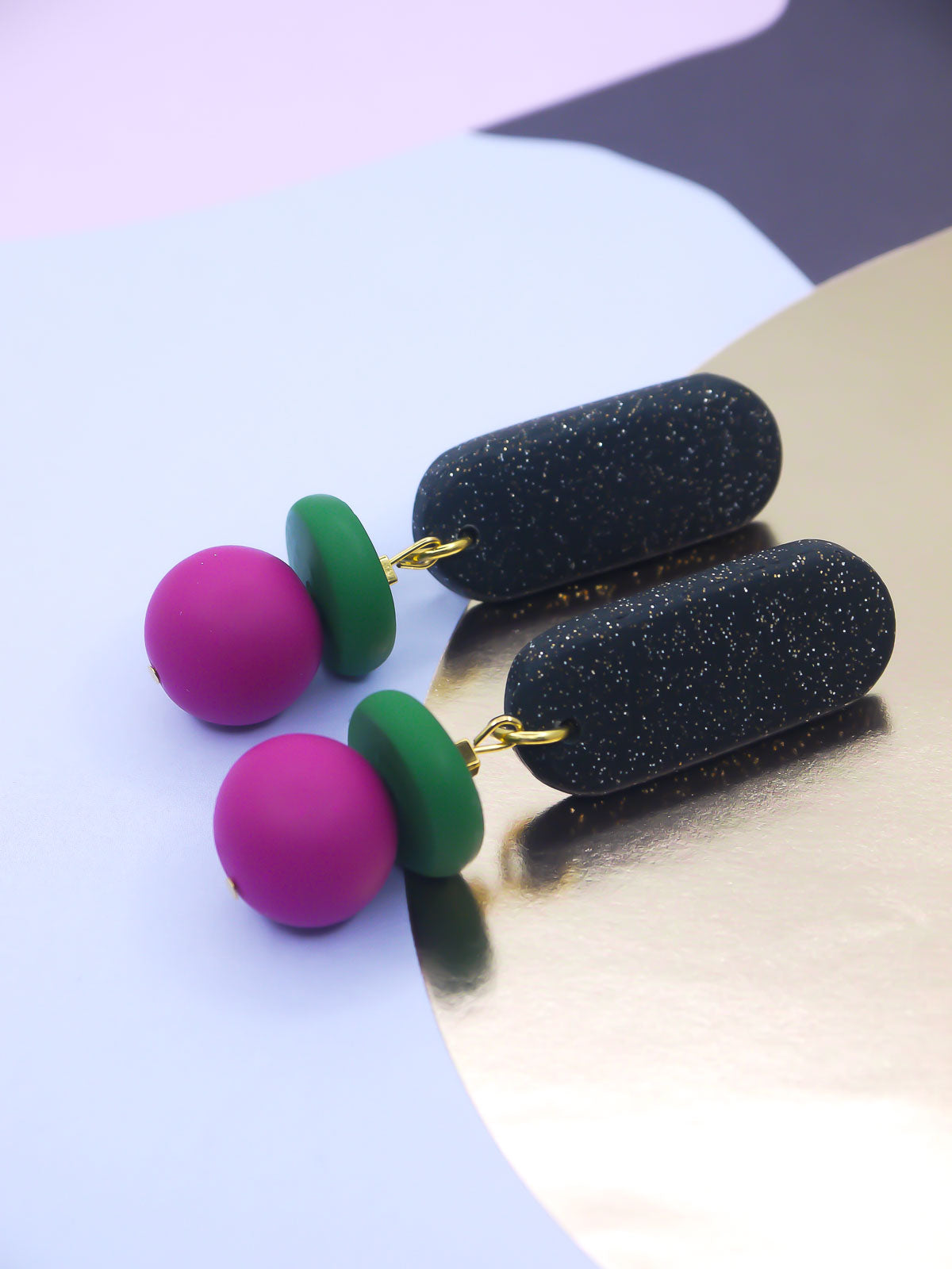 Colorful earrings with pink, green, and black on a reflective surface