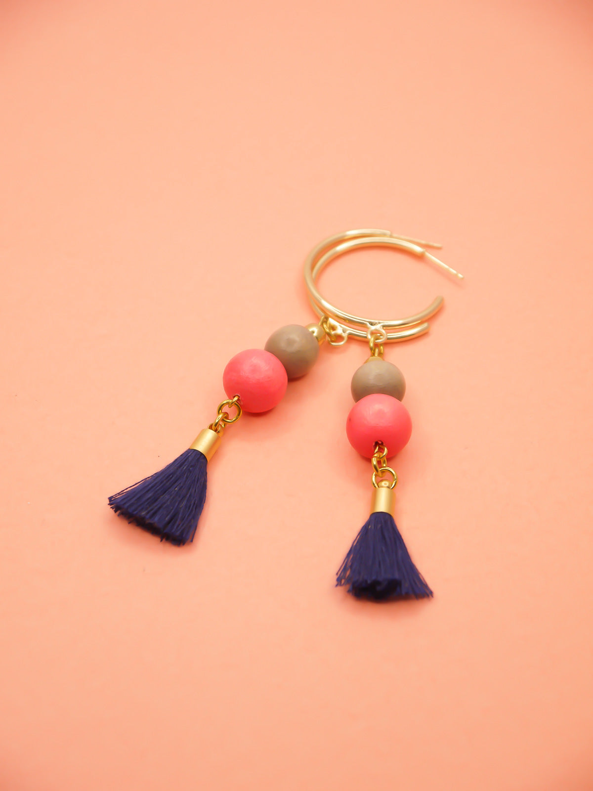 Gold hoop beaded tassel earrings with wooden beads in salmon and light grey with a navy blue tassel and gold hoops