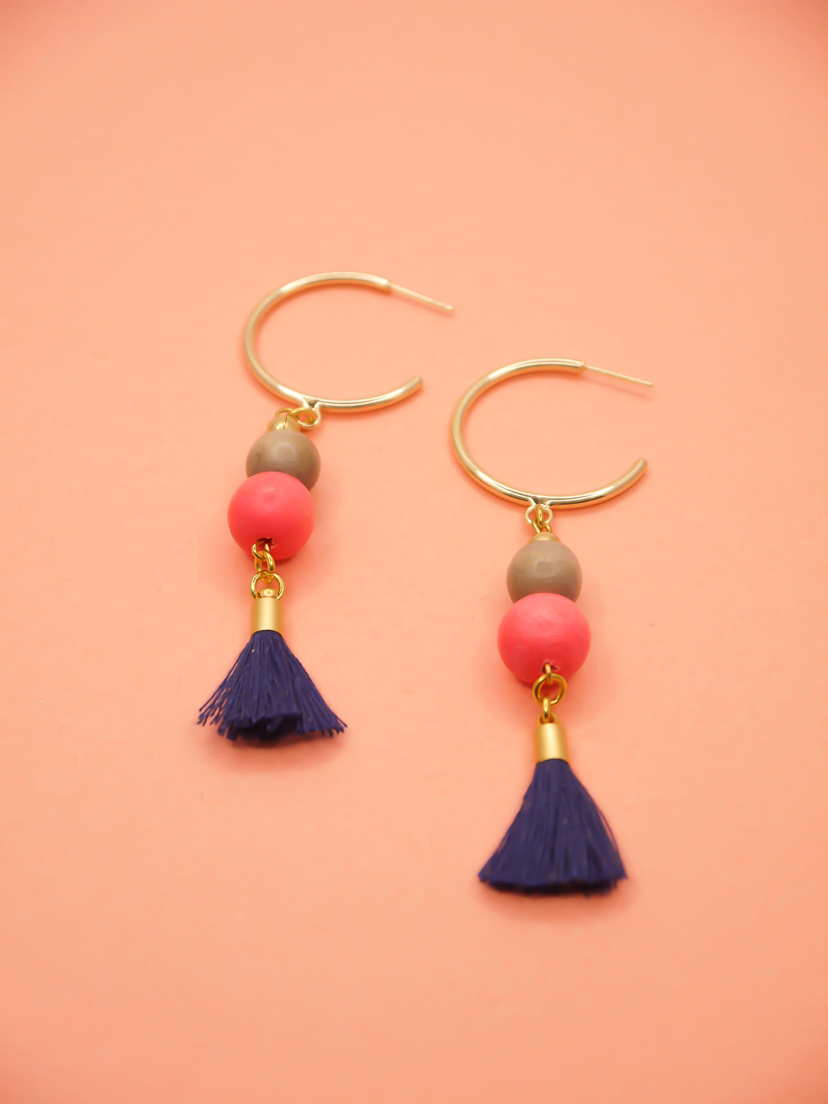 Gold hoop beaded tassel earrings with wooden beads in salmon and light grey with a navy blue tassel and gold hoops