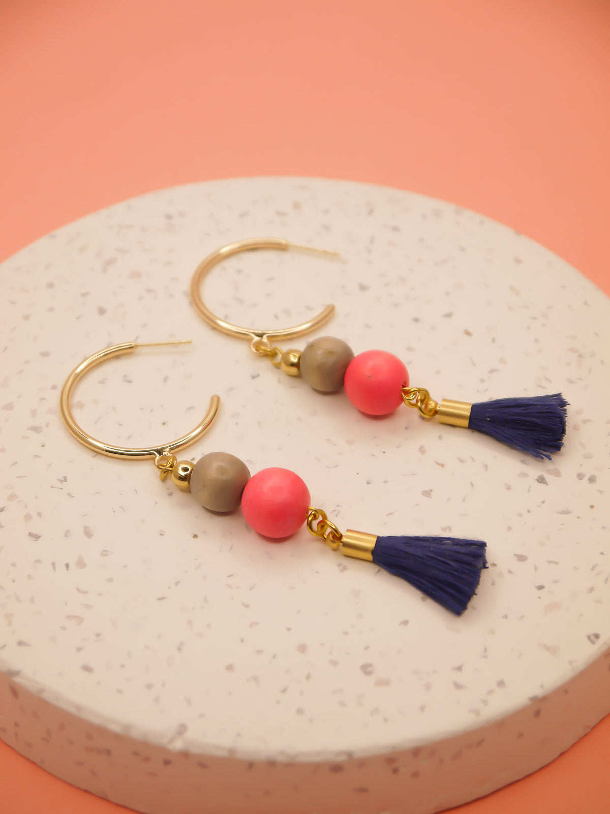 Gold hoop beaded tassel earrings with wooden beads in salmon and light grey with a navy blue tassel and gold hoops