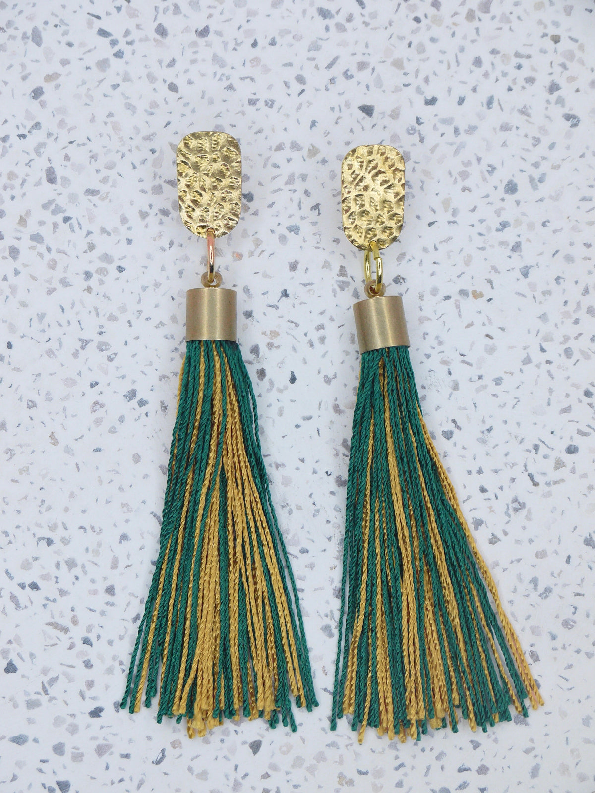 Green and gold tassel earrings with a textured brass stud on a marbled white surface 