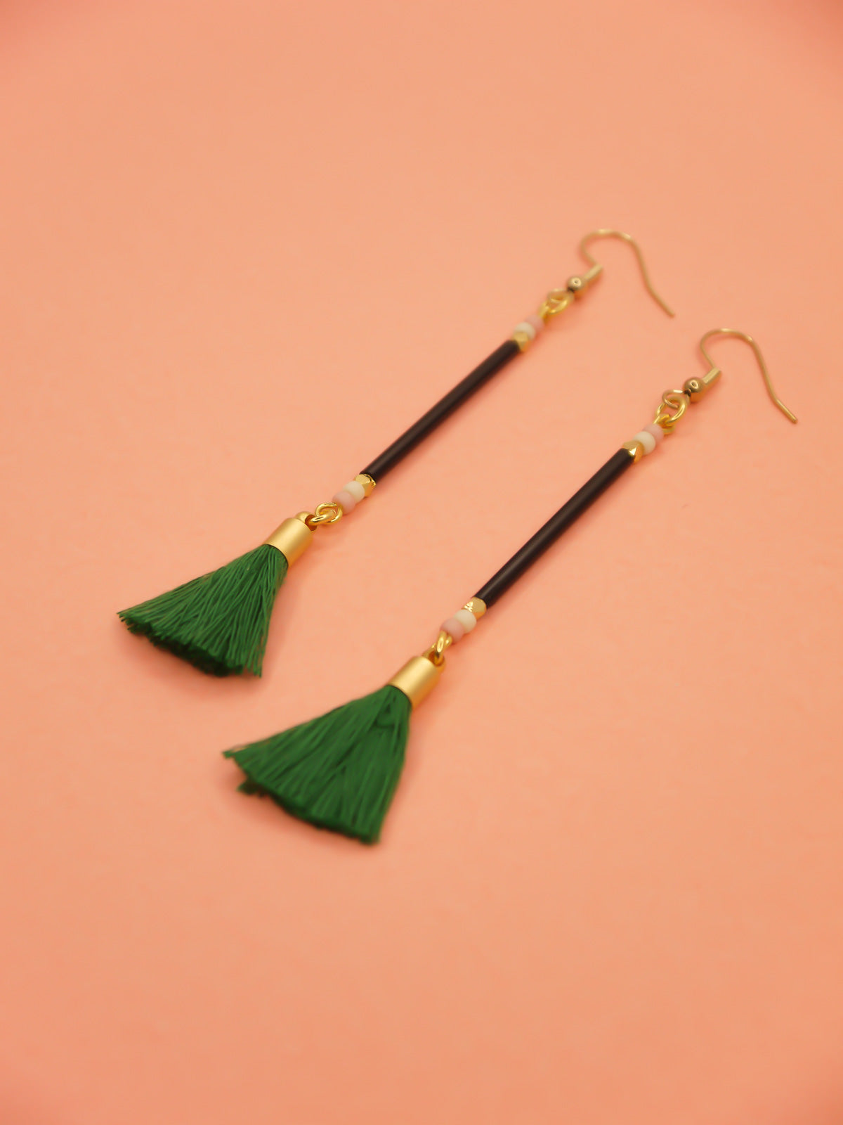 Long delicate bead stick dangle earrings with black glass tube beads & contrasting seed beads in pink & white. Paired with a green cotton tassel & hung from gold plated nickel free ear wires