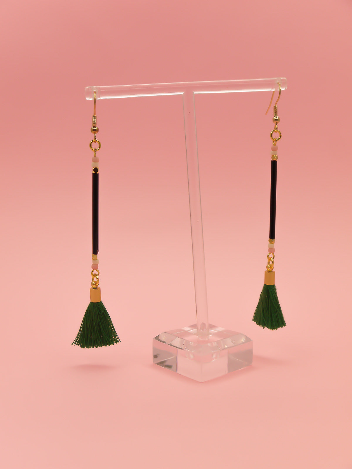 Long delicate bead stick dangle earrings with black glass tube beads & contrasting seed beads in pink & white. Paired with a green cotton tassel & hung from gold plated nickel free ear wires