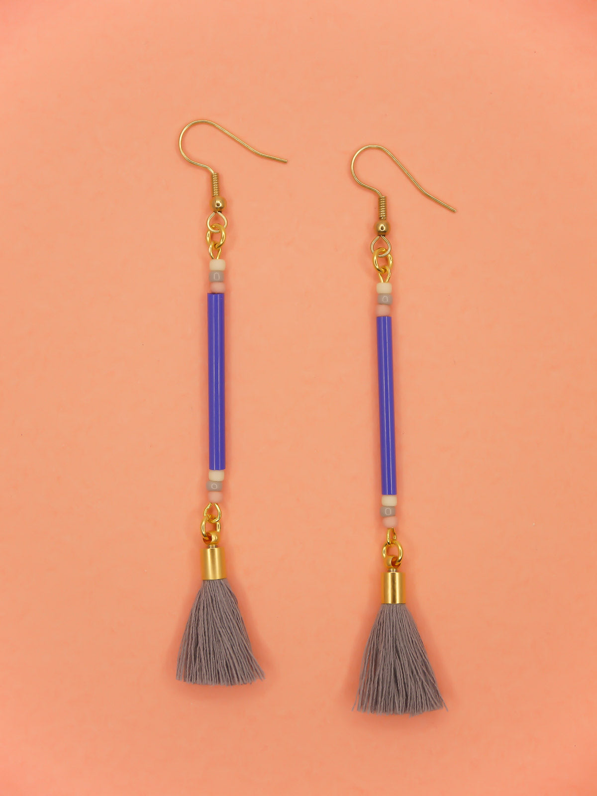 Long delicate bead stick dangle earrings featuring blue tube beads with contrasting seed beads in pink, white & grey, paired with a grey cotton tassel & hung from gold plated nickel free ear wires