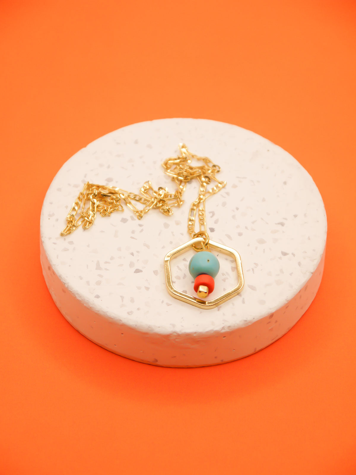 Geometric necklace comprising of a gold plated hexagon charm with a turquoise gemstone bead in the centre with an orange ceramic and brass square bead. Hung from a 24k shiny gold faceted curb chain with extender