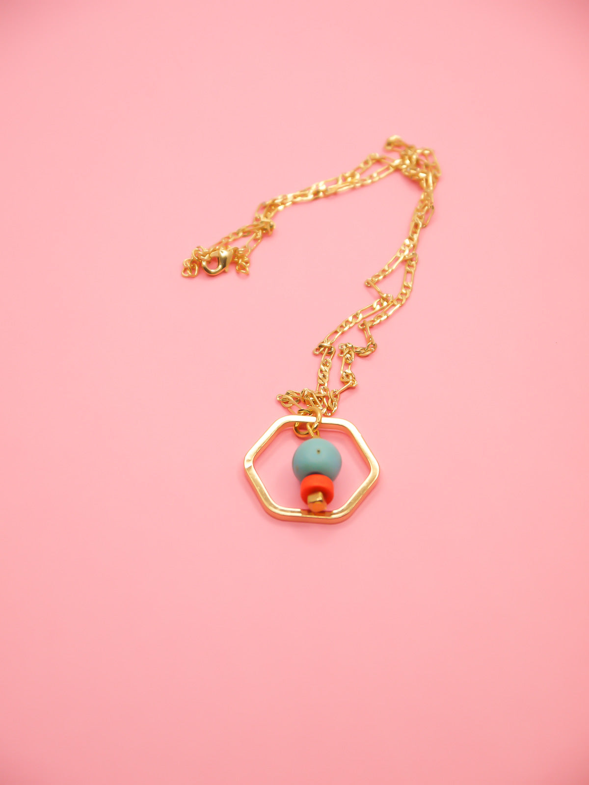 Geometric necklace comprising of a gold plated hexagon charm with a turquoise gemstone bead in the centre with an orange ceramic and brass square bead. Hung from a 24k shiny gold faceted curb chain with extender