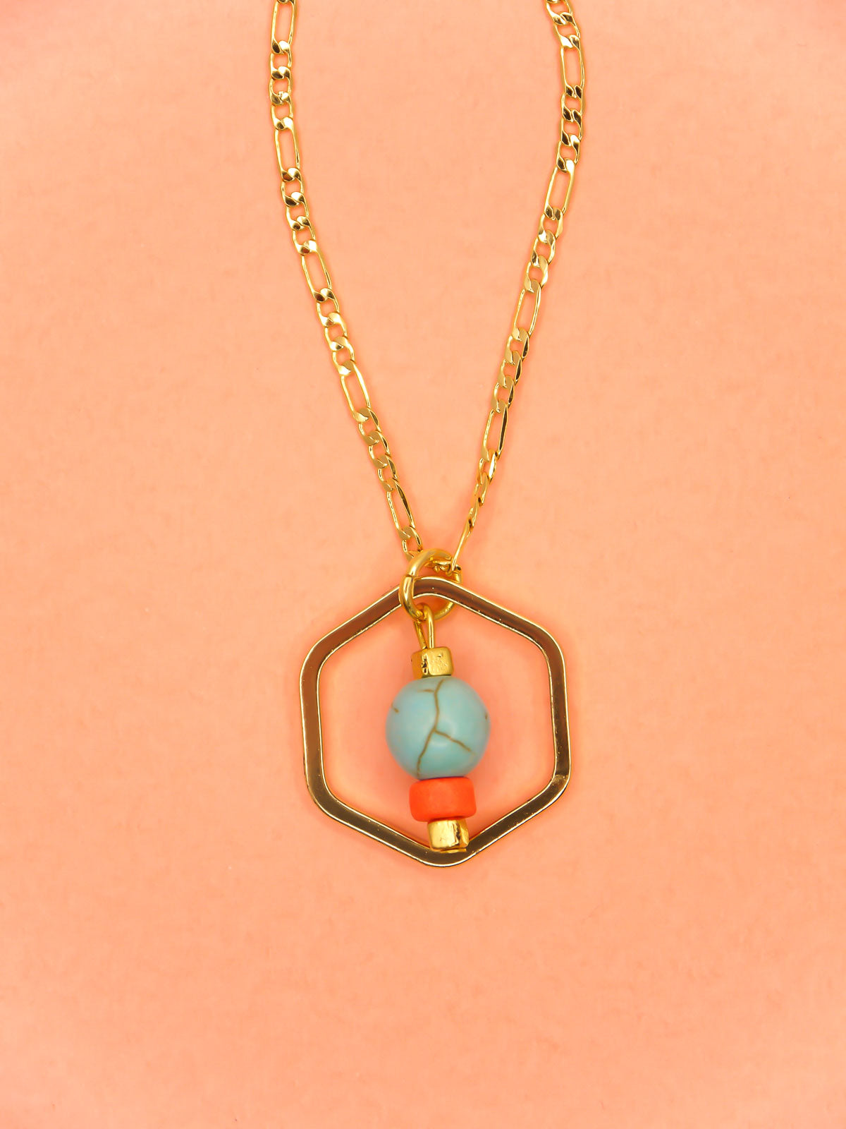 Geometric necklace comprising of a gold plated hexagon charm with a turquoise gemstone bead in the centre with an orange ceramic and brass square bead. Hung from a 24k shiny gold faceted curb chain with extender