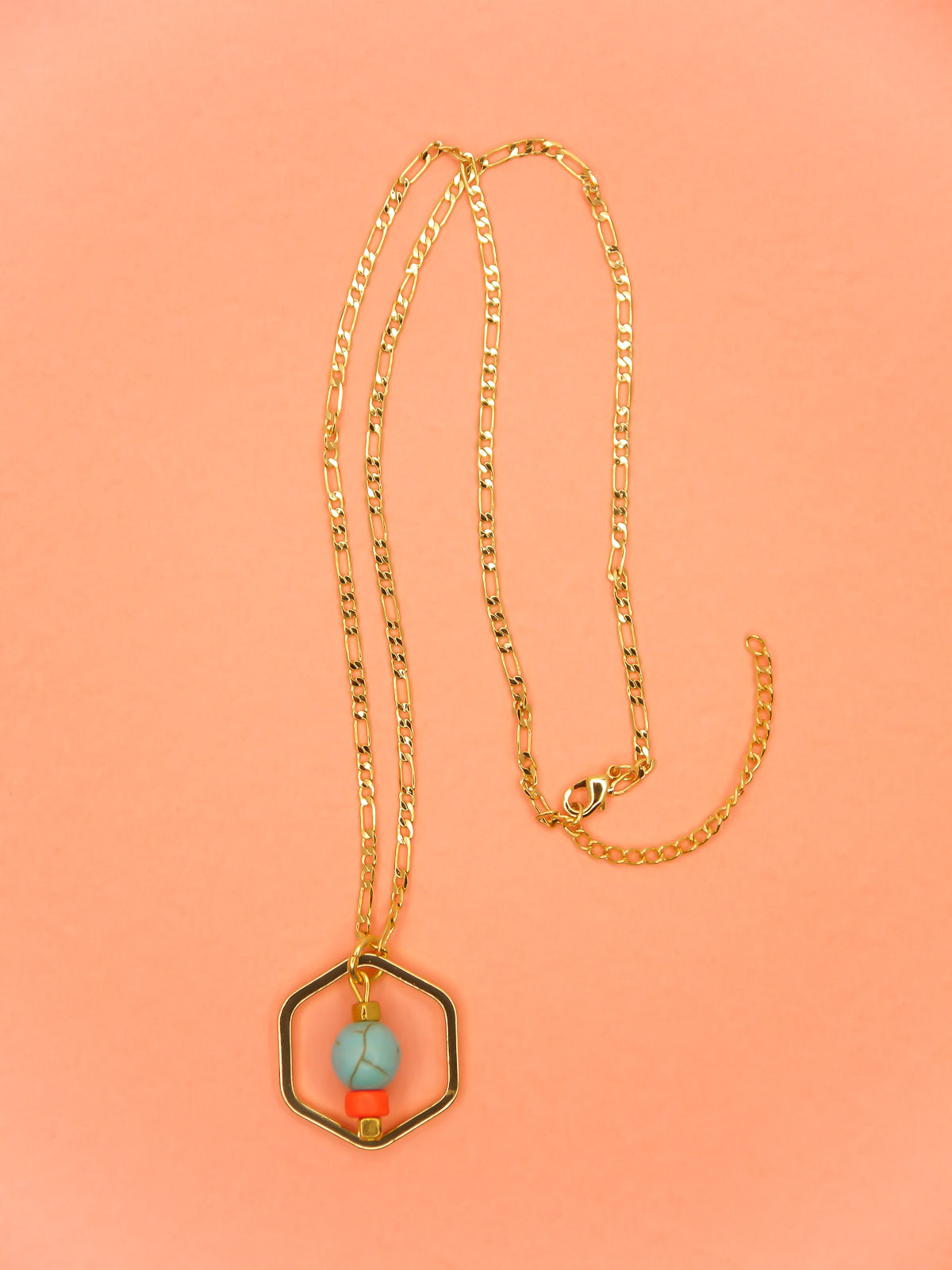 Geometric necklace comprising of a gold plated hexagon charm with a turquoise gemstone bead in the centre with an orange ceramic and brass square bead. Hung from a 24k shiny gold faceted curb chain with extender