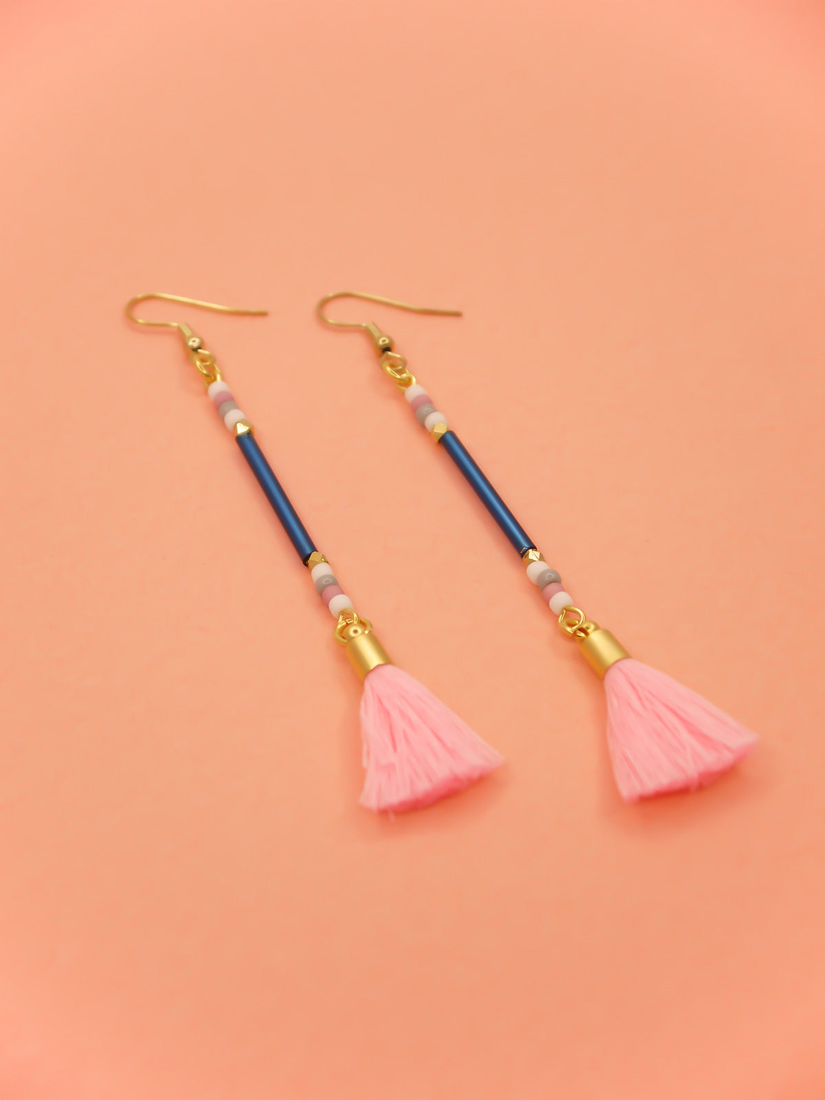 Long beaded tassel earrings with blue glass tube beads and white, pink & grey seed beads with a light pink cotton tassel and hung from gold plated nickel free ear wires