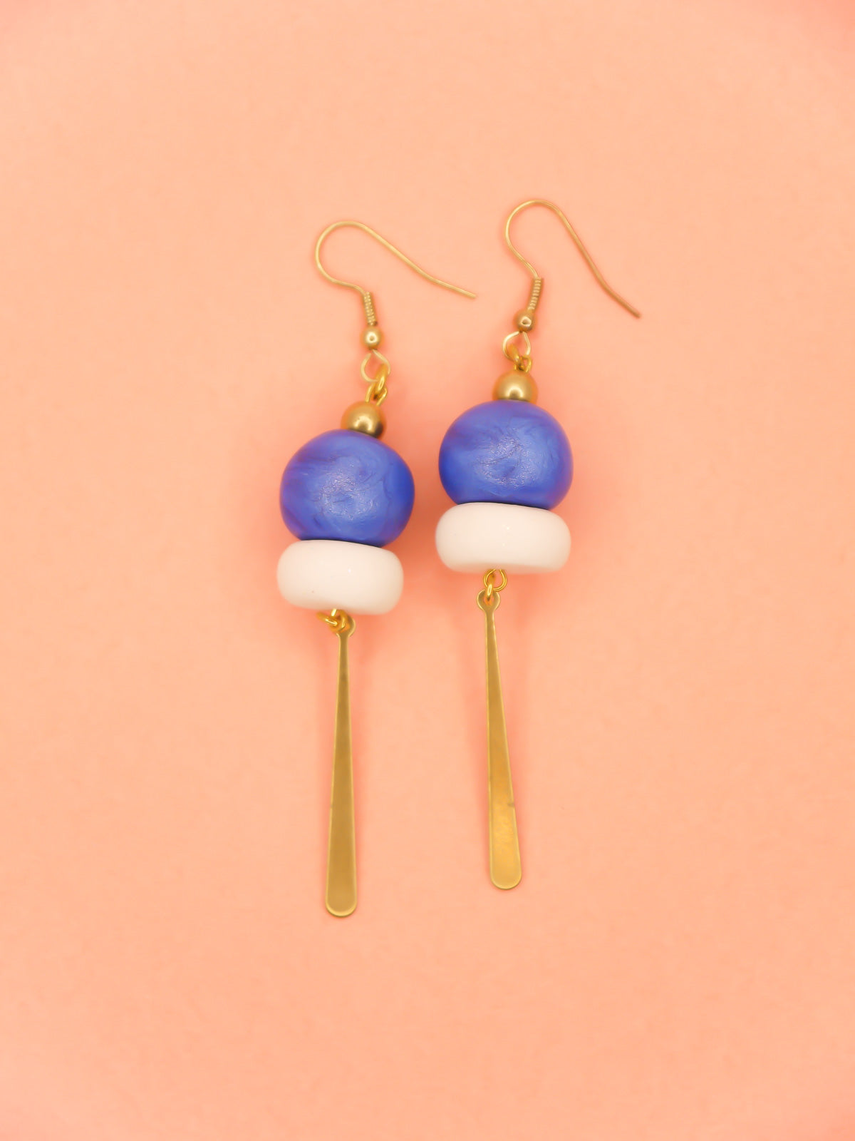 Metallic bead dangle earrings with two hand rolled metallic beads in blue and  white glitter with a brass stick charm, hung from gold plated ear wires