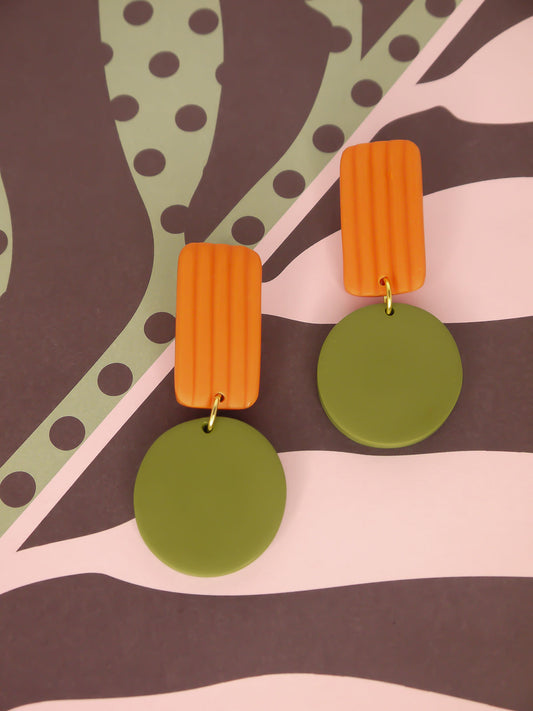 Pair of geometric earrings with orange striped rectangles and green circular pendants on a patterned background
