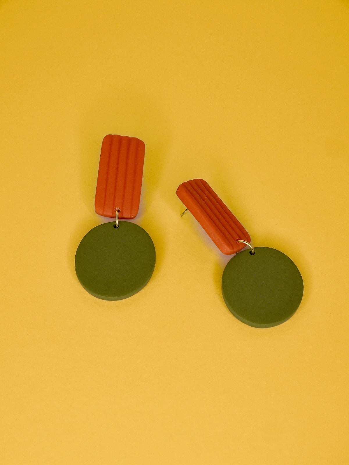 Pair of geometric earrings with green round pendants and orange rectangular striped tops on a yellow background