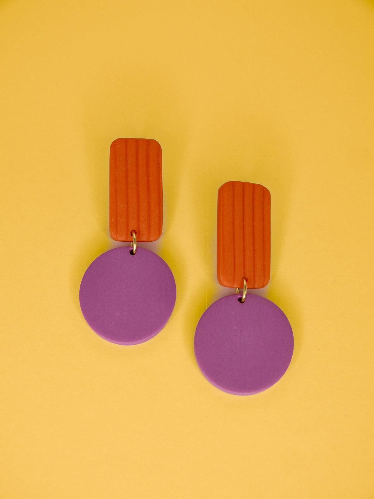 Pair of geometric earrings with striped orange rectangles and purple circles on a yellow background