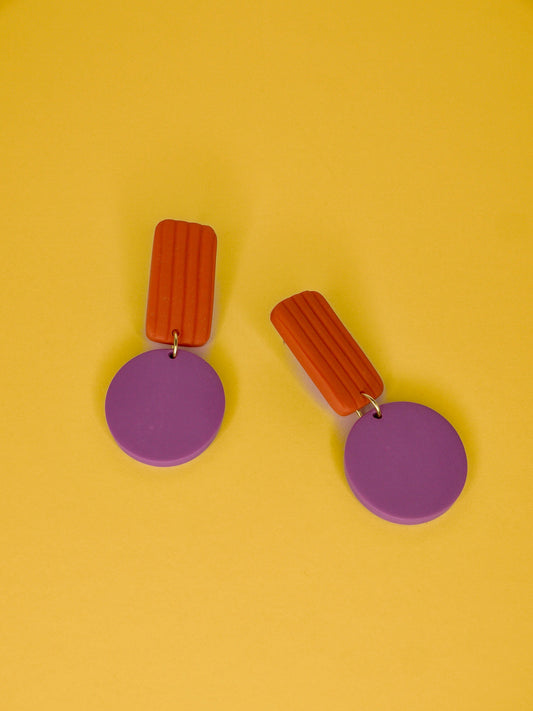 Pair of geometric earrings with striped orange rectangles and purple circles on a yellow background
