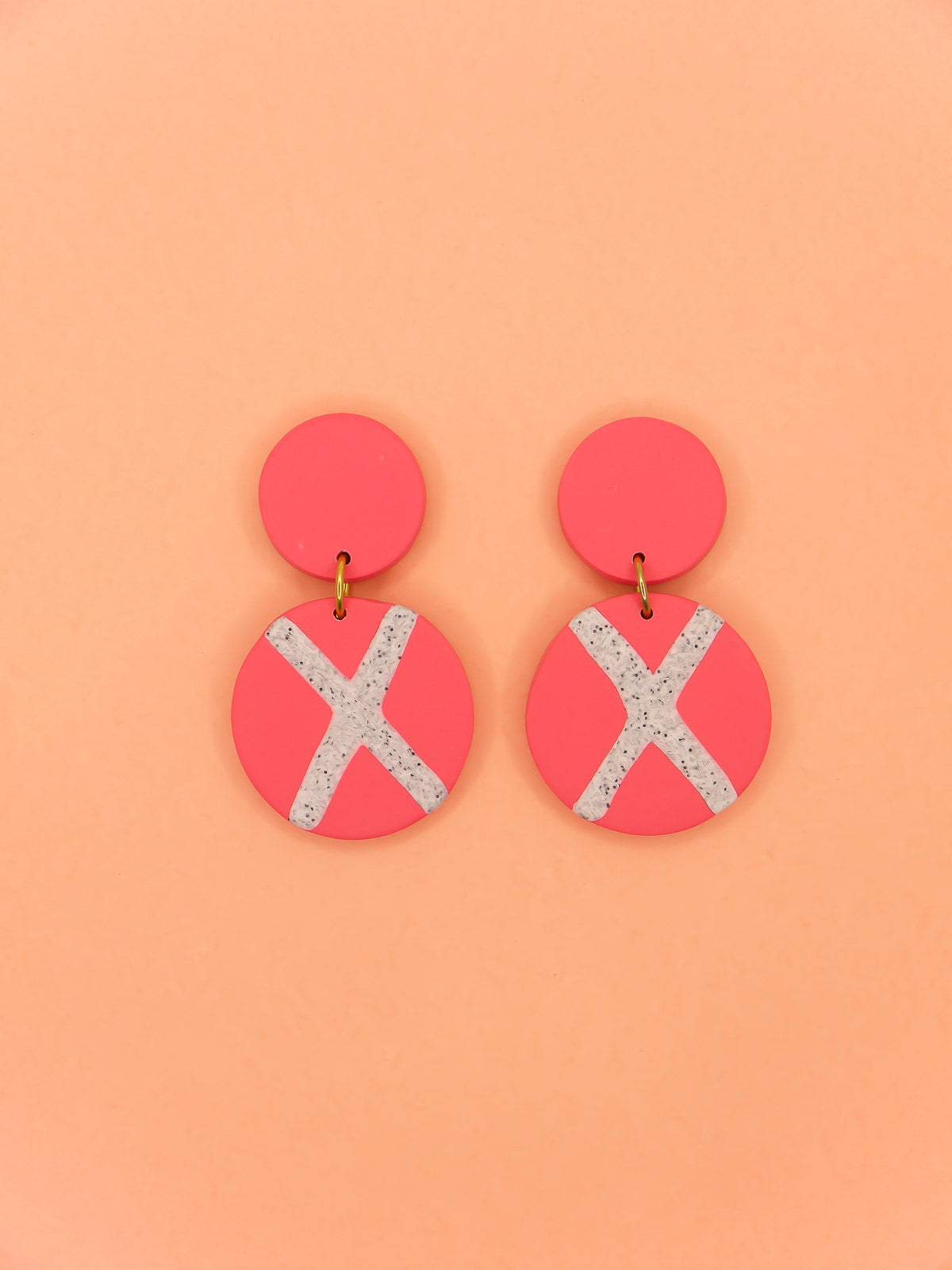 Polymer clay dangle statement earrings with a pink stud connected to a pink circle with a granite cross in the centre