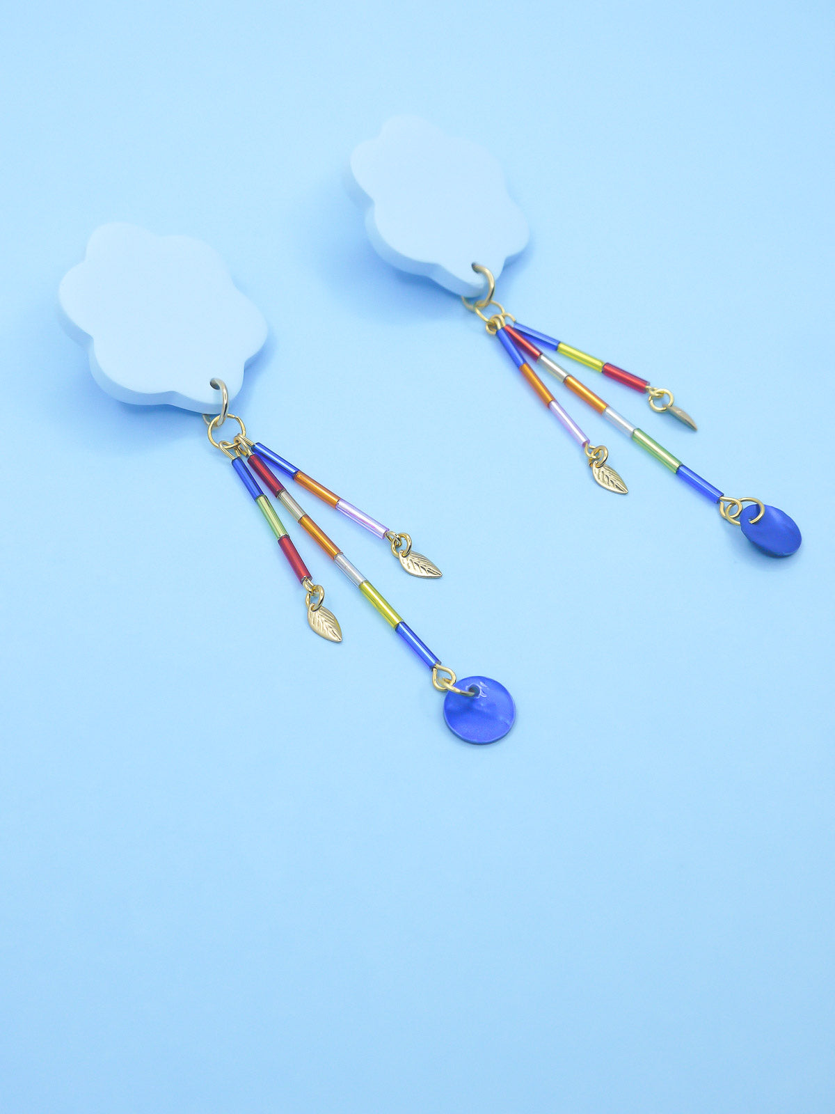 Colourful earrings of blue clouds with glass dangle tube beads on a pink background