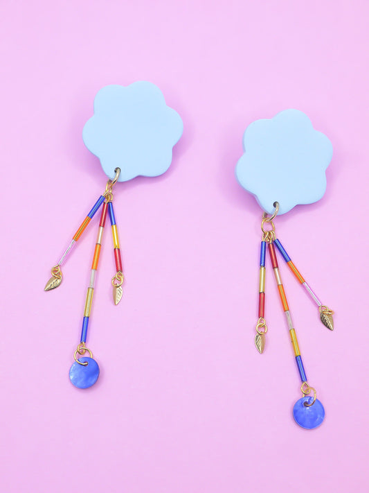 Colourful earrings of blue clouds with glass dangle tube beads on a pink background