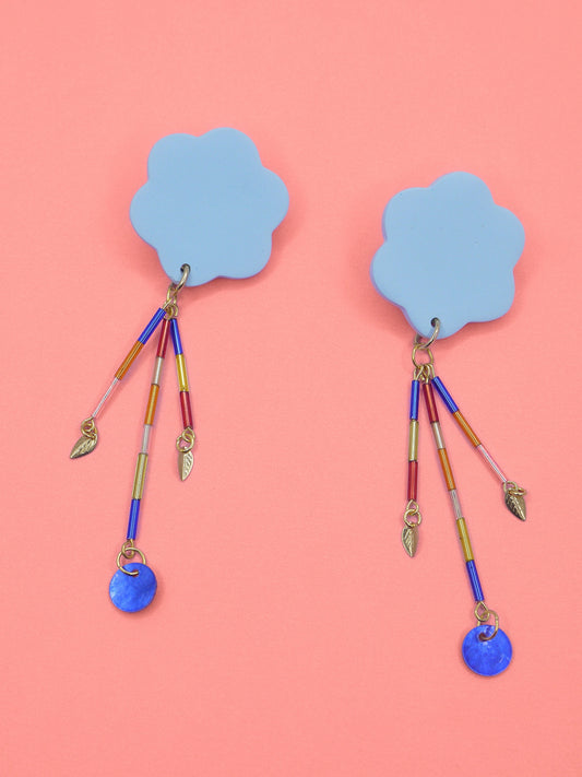 Colourful earrings of blue clouds with glass dangle tube beads on a pink background