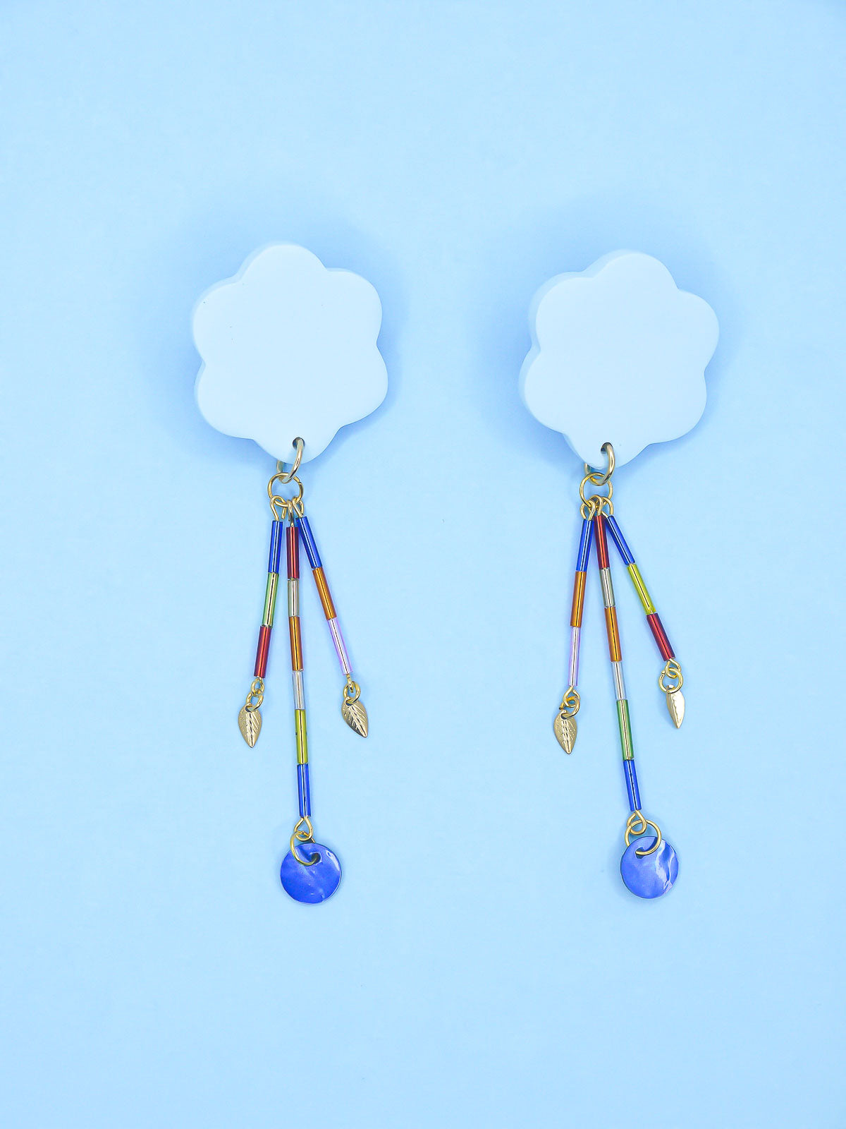 Colourful earrings of blue clouds with glass dangle tube beads on a pink background