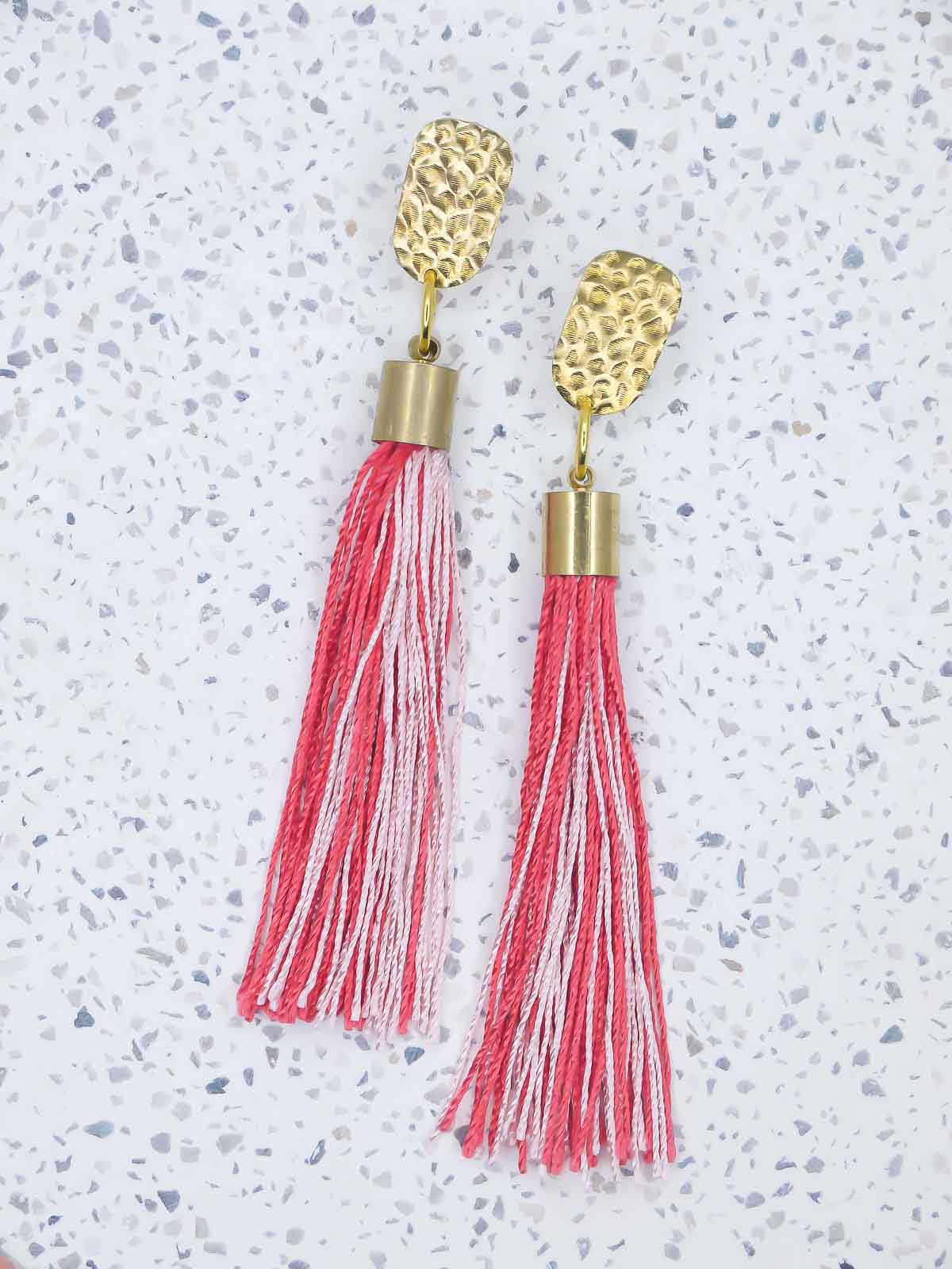 Red & pink tassel dangle earrings with a textured brass stud on a marble background