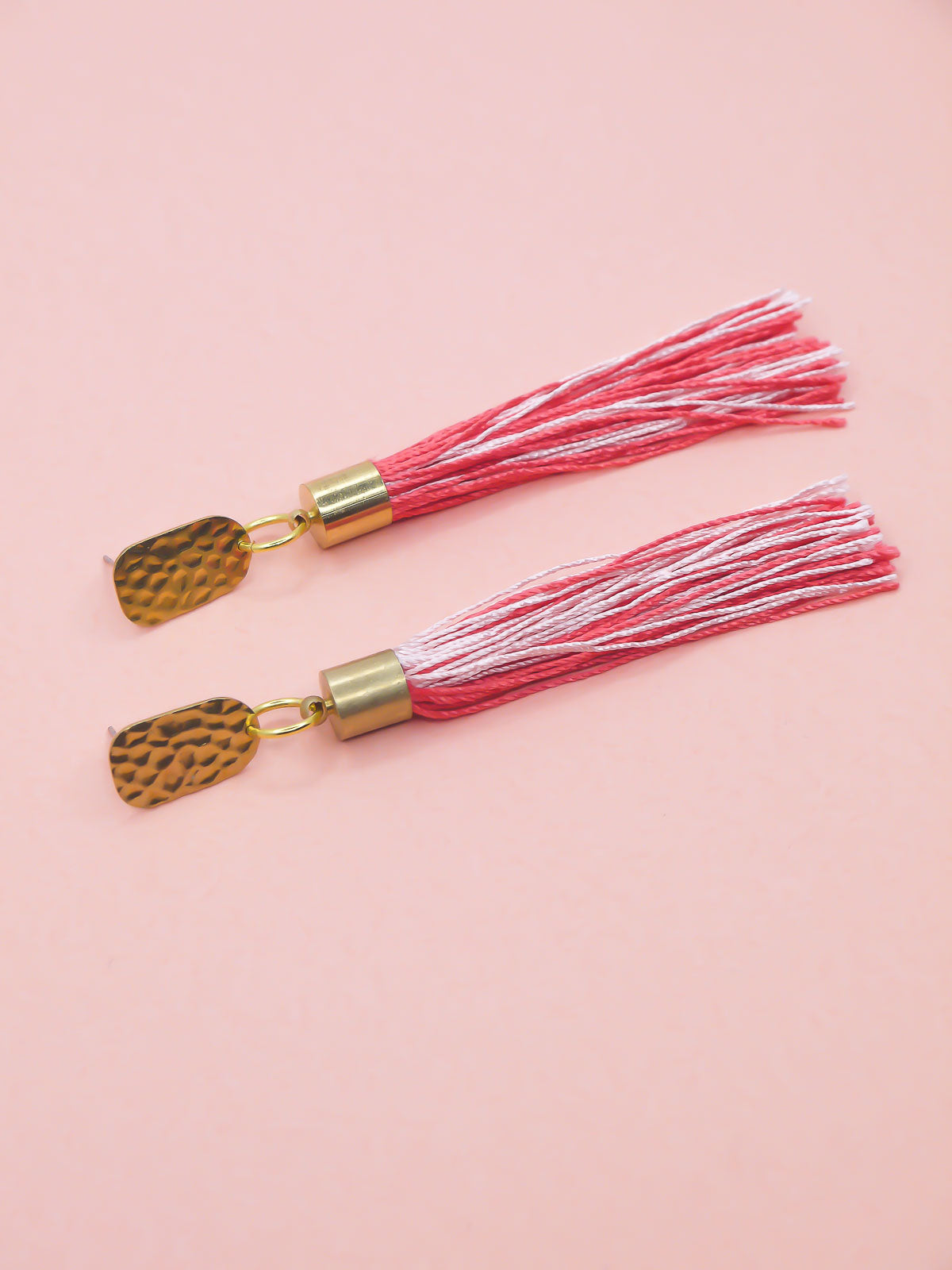 Pink & red tassel earrings with textured brass studs on a pink background