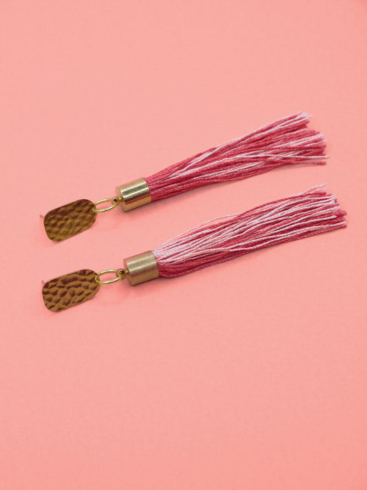 Pink & red tassel earrings with textured brass studs on a pink background
