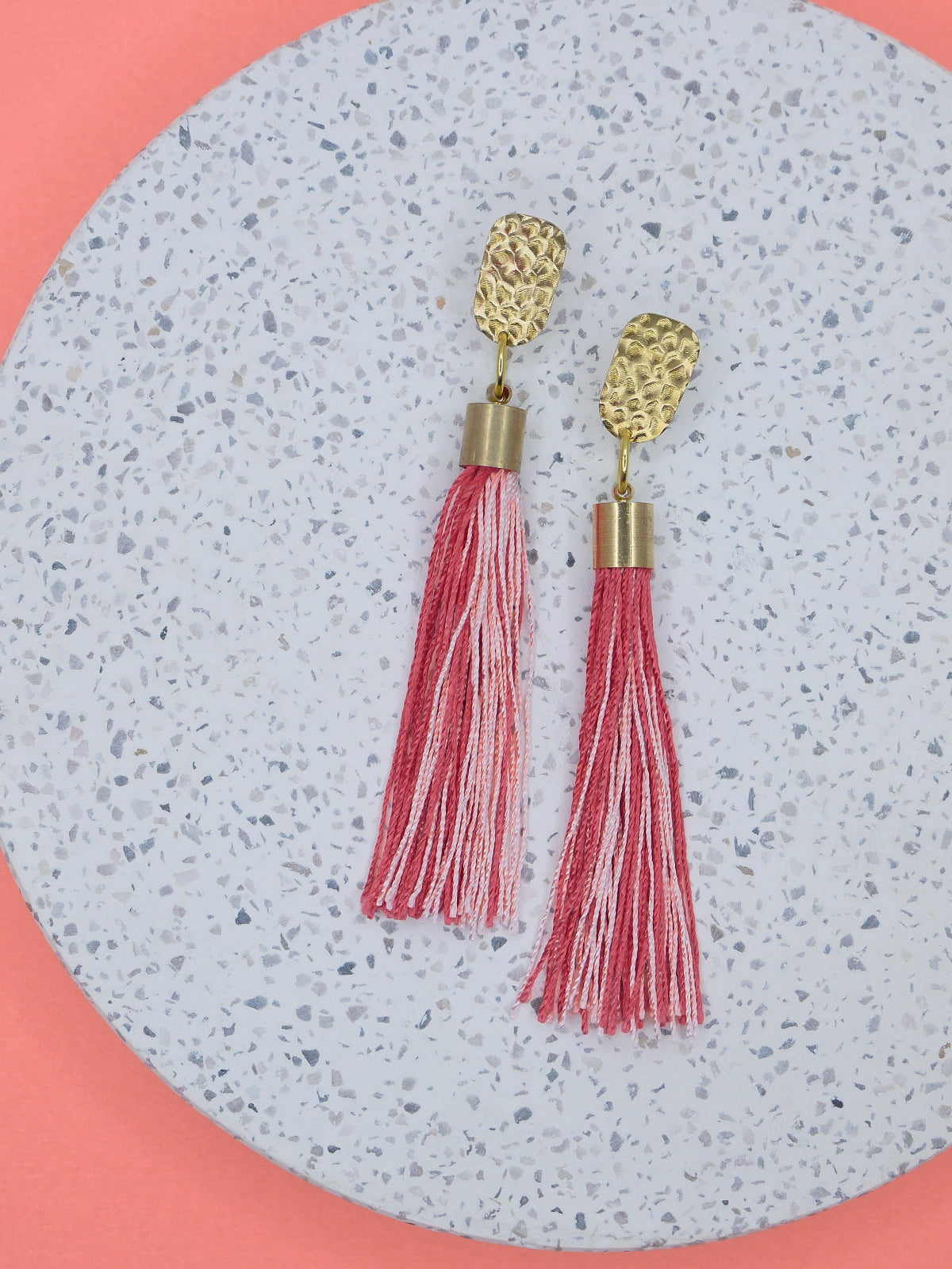 Red & pink tassel dangle earrings with a textured brass stud on a marble background