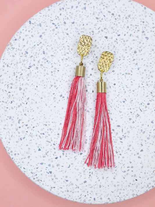 Red & pink tassel dangle earrings with a textured brass stud on a marble background