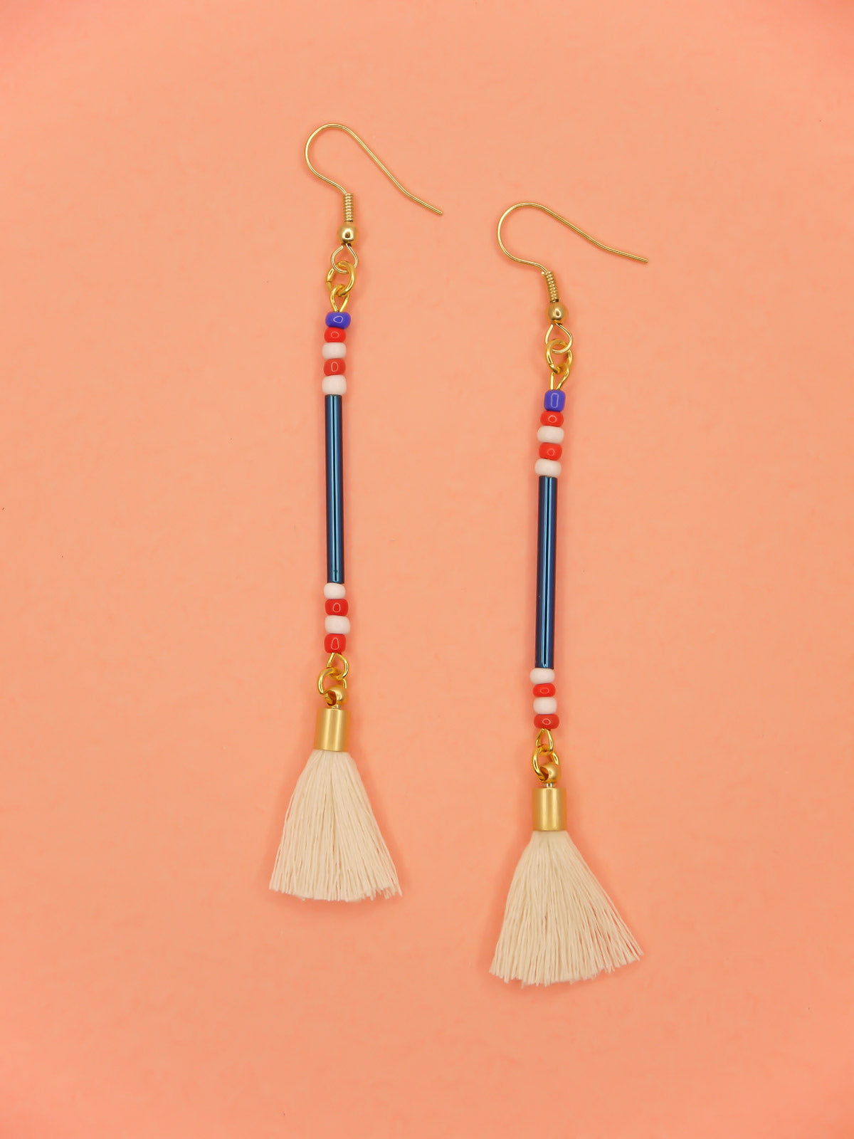 Lightweight delicate long beaded dangle earrings with a blue metallic tube bead and contrasting seed beads in red, white & blue, paired with a white cotton tassel. Hung from gold plated nickel free ear wires. 