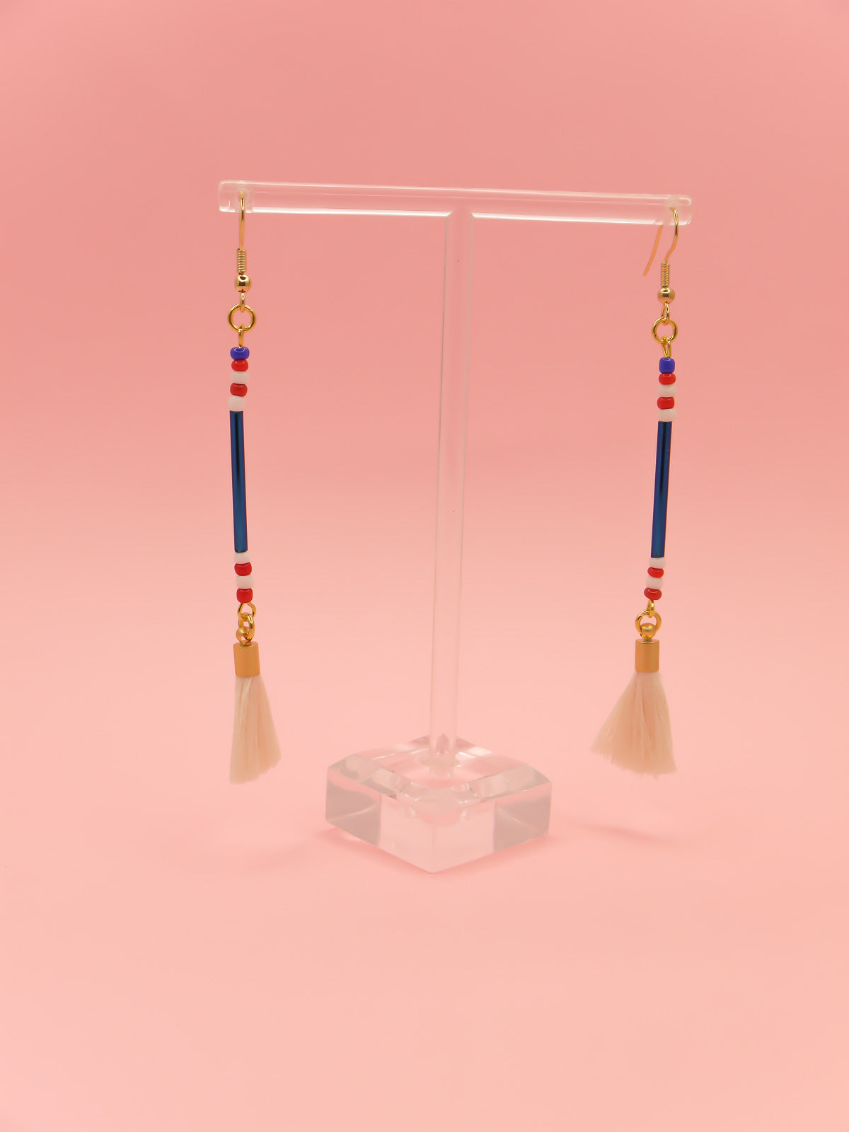 Lightweight delicate long beaded dangle earrings with a blue metallic tube bead and contrasting seed beads in red, white & blue, paired with a white cotton tassel. Hung from gold plated nickel free ear wires. 