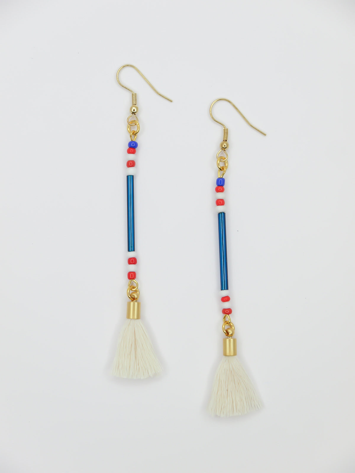 Lightweight delicate long beaded dangle earrings with a blue metallic tube bead and contrasting seed beads in red, white & blue, paired with a white cotton tassel. Hung from gold plated nickel free ear wires. 