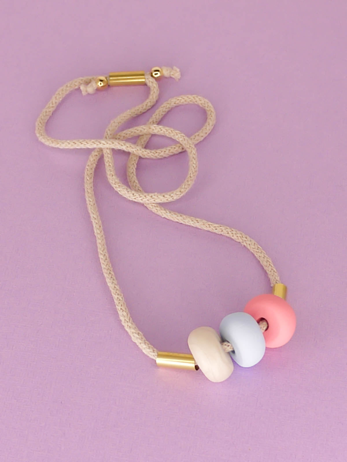 Modern lightweight polymer clay bead necklace comprising of three handmade beads in pink, ice blue and marble with two brass tubes either side strung on an adjustable beige cotton rope to wear short or long.