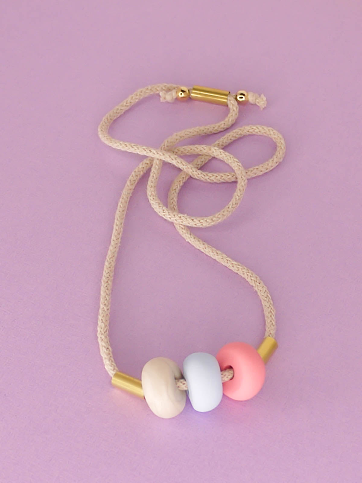 Modern lightweight polymer clay bead necklace comprising of three handmade beads in pink, ice blue and marble with two brass tubes either side strung on an adjustable beige cotton rope to wear short or long.