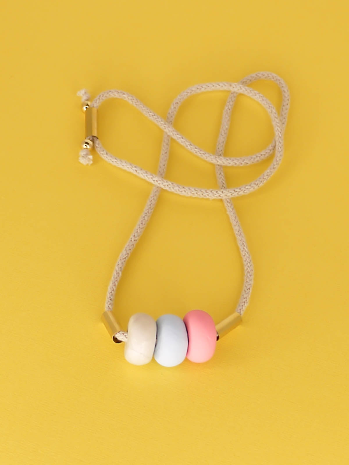 Modern lightweight polymer clay bead necklace comprising of three handmade beads in pink, ice blue and marble with two brass tubes either side strung on an adjustable beige cotton rope to wear short or long.