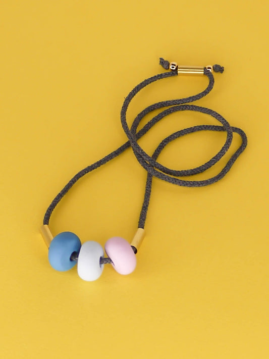 Lightweight statement bead necklace made up of grey cotton rope which is adjustable through a brass slider so it can be worn long or short. Comprised of 3 handmade polymer clay beads in blue, ice blue & lilac with 2 brass tube beads.