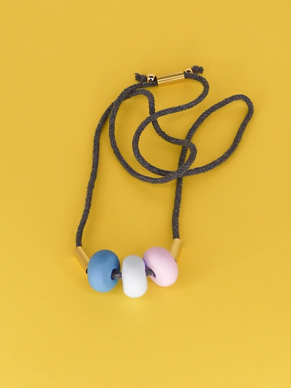 Lightweight statement bead necklace made up of grey cotton rope which is adjustable through a brass slider so it can be worn long or short. Comprised of 3 handmade polymer clay beads in blue, ice blue & lilac with 2 brass tube beads.