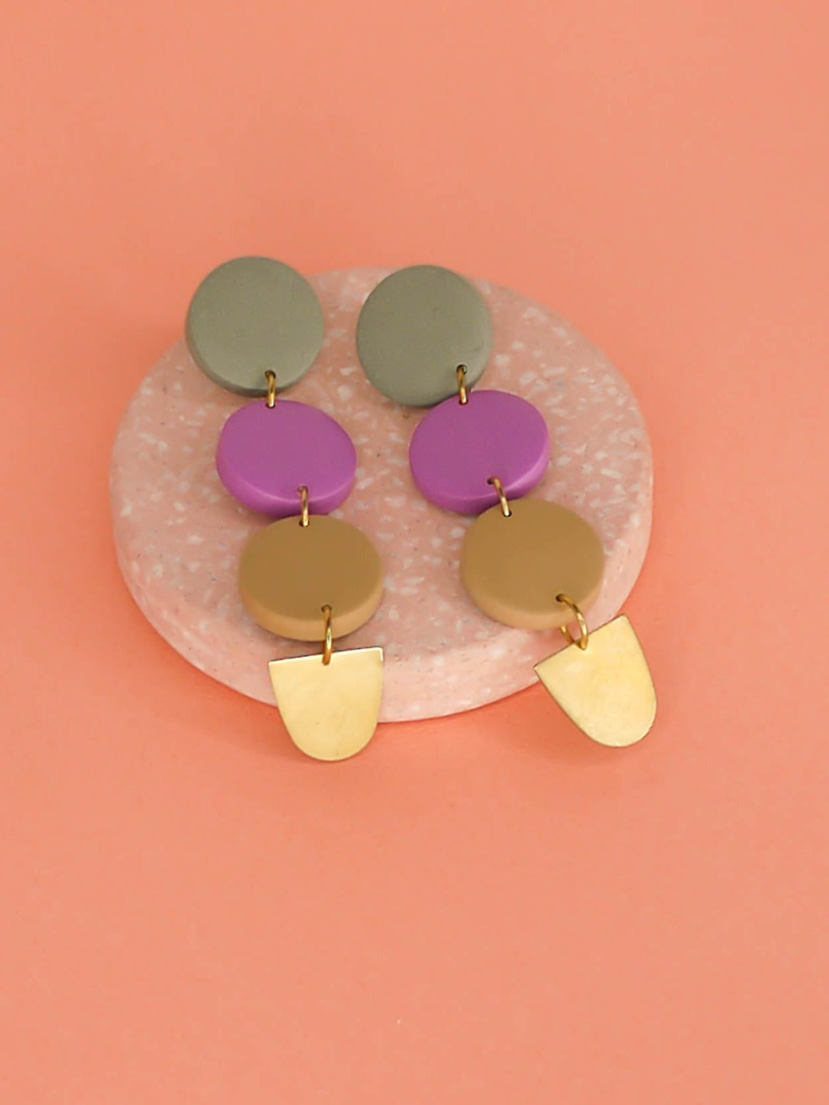 4 tier long colour block circle dangle statement earrings with 3 connected circles made from polymer clay in sage, purple & beige, with a brass semi circle charm dangling on the bottom and stainless steel earring posts.