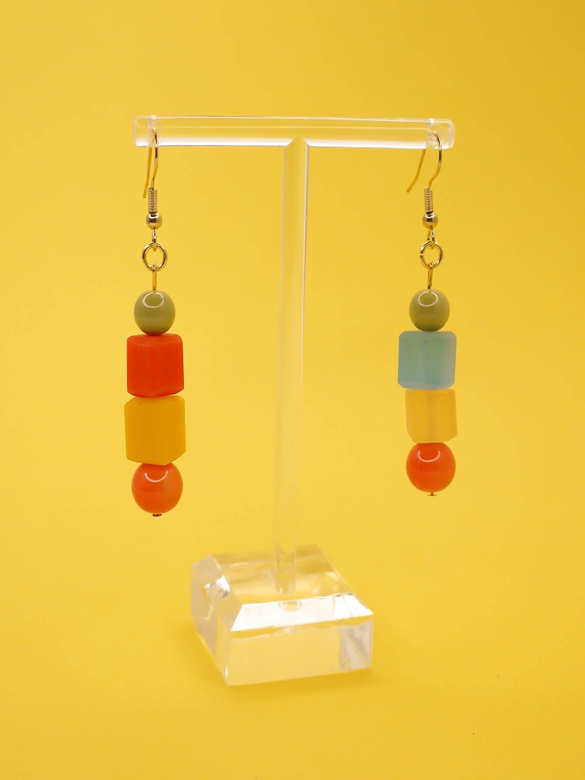 Geometric asymmetrical coloured bead earrings with glass circle beads in orange, square resin beads in orange, yellow and blue , topped with a glass bead in sage green. Hung from brass earring hooks.