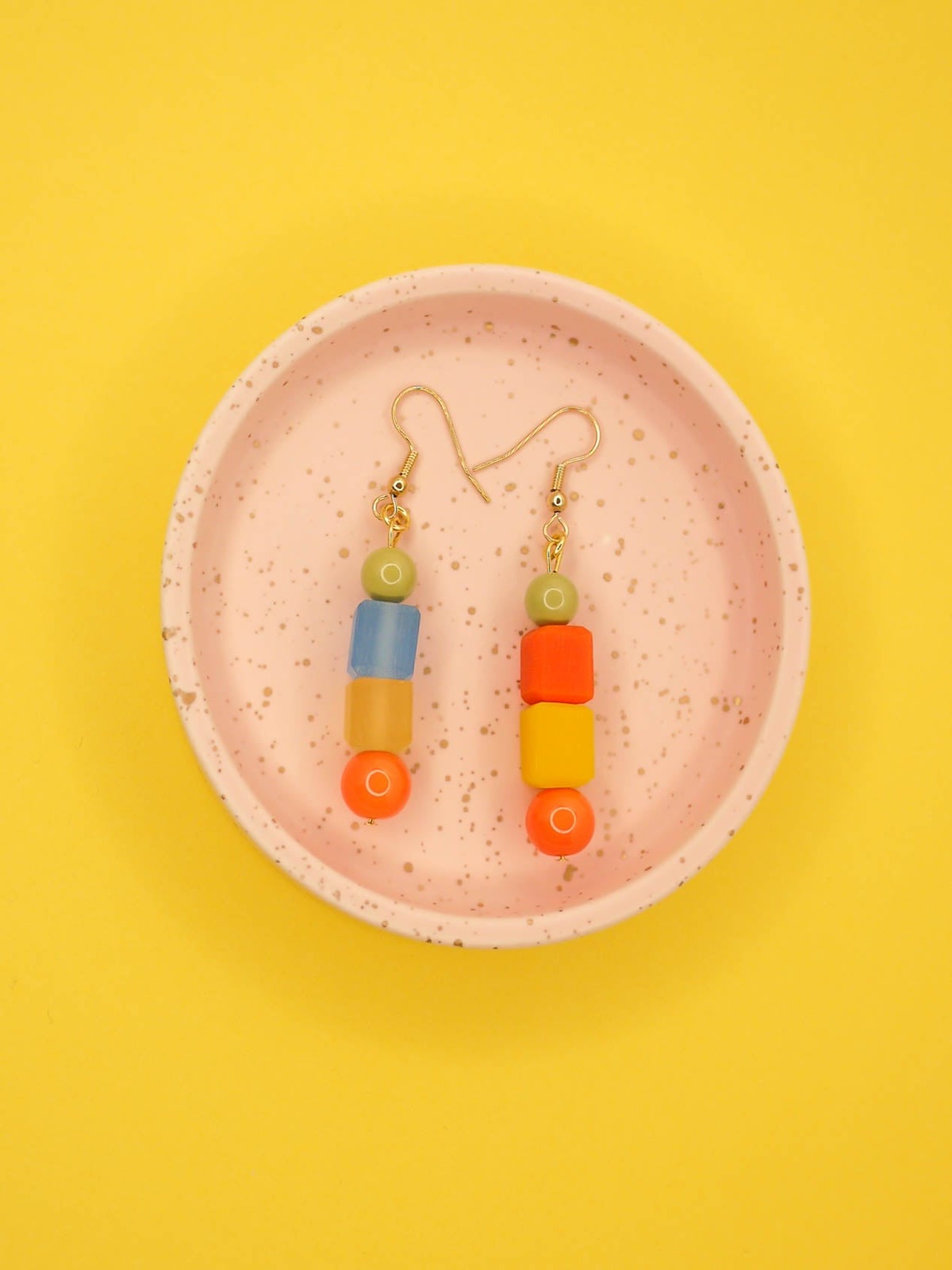 Geometric asymmetrical coloured bead earrings with glass circle beads in orange, square resin beads in orange, yellow and blue , topped with a glass bead in sage green. Hung from brass earring hooks.