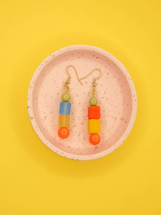 Geometric asymmetrical coloured bead earrings with glass circle beads in orange, square resin beads in orange, yellow and blue , topped with a glass bead in sage green. Hung from brass earring hooks.