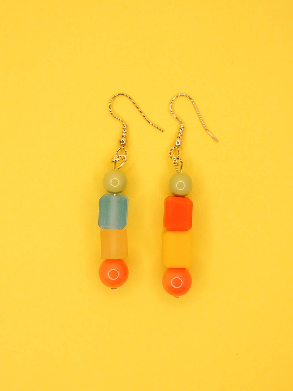 Geometric asymmetrical coloured bead earrings with glass circle beads in orange, square resin beads in orange, yellow and blue , topped with a glass bead in sage green. Hung from brass earring hooks.