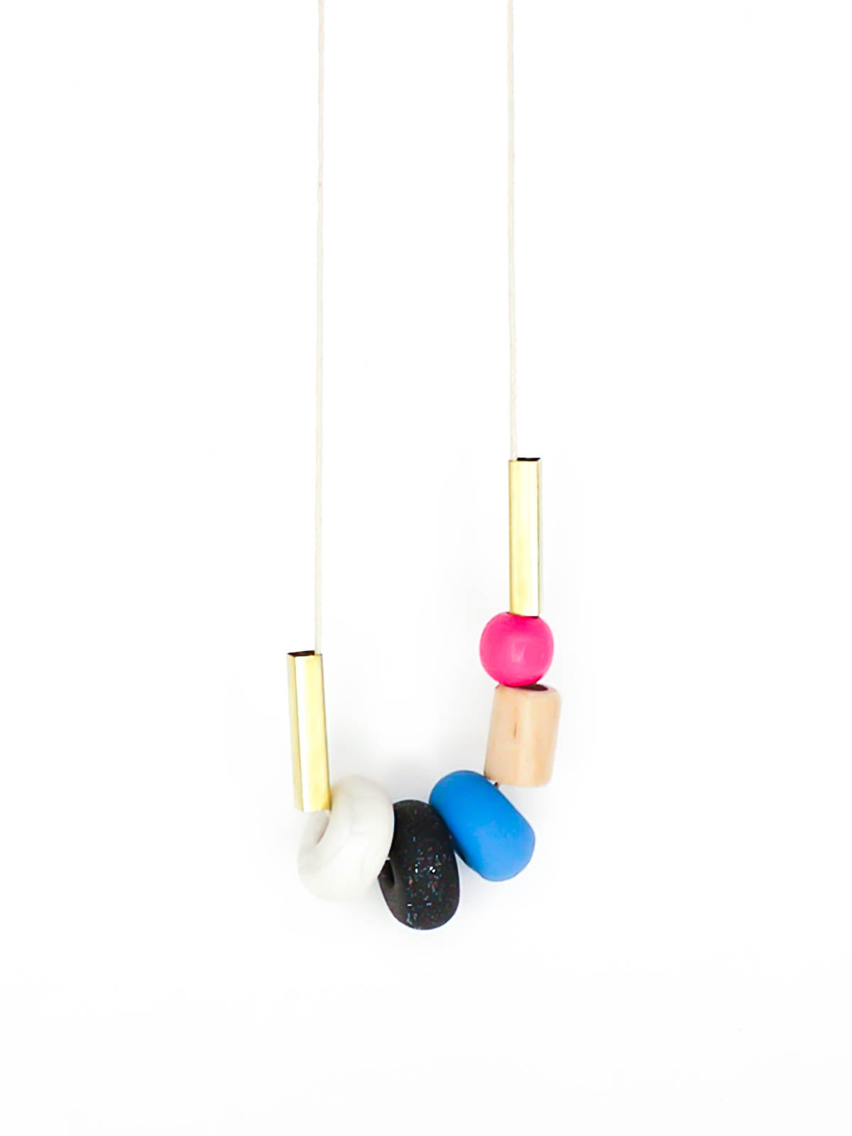 Lightweight geometric colourful bead necklace with 3 handmade polymer clay beads in marble, blue & black glitter- wood tube bead & pink wood bead, brass tube beads on either side, strung on a cotton cord with a blue wood bead knotted at the end