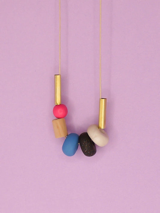 Lightweight geometric colourful bead necklace with 3 handmade polymer clay beads in marble, blue & black glitter- wood tube bead & pink wood bead, brass tube beads on either side, strung on a cotton cord with a blue wood bead knotted at the end