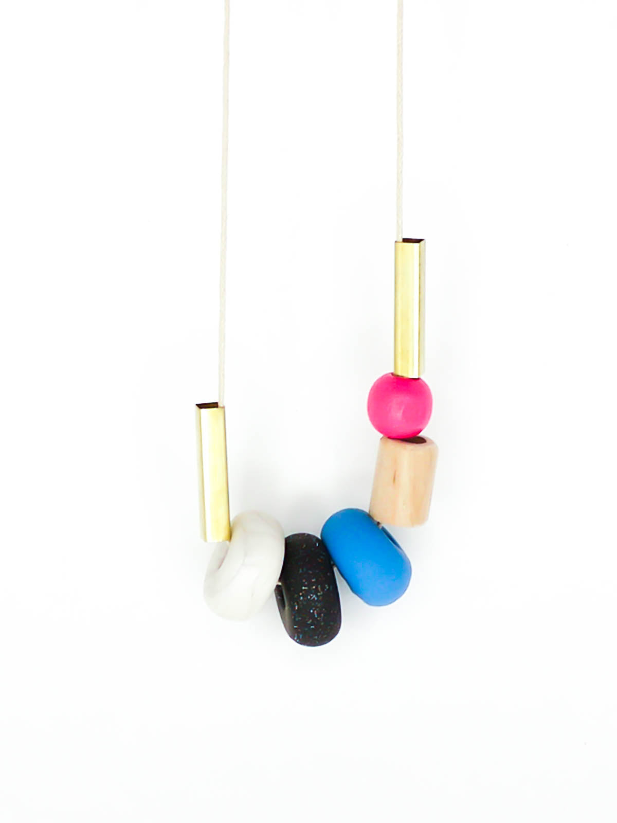 Lightweight geometric colourful bead necklace with 3 handmade polymer clay beads in marble, blue & black glitter- wood tube bead & pink wood bead, brass tube beads on either side, strung on a cotton cord with a blue wood bead knotted at the end