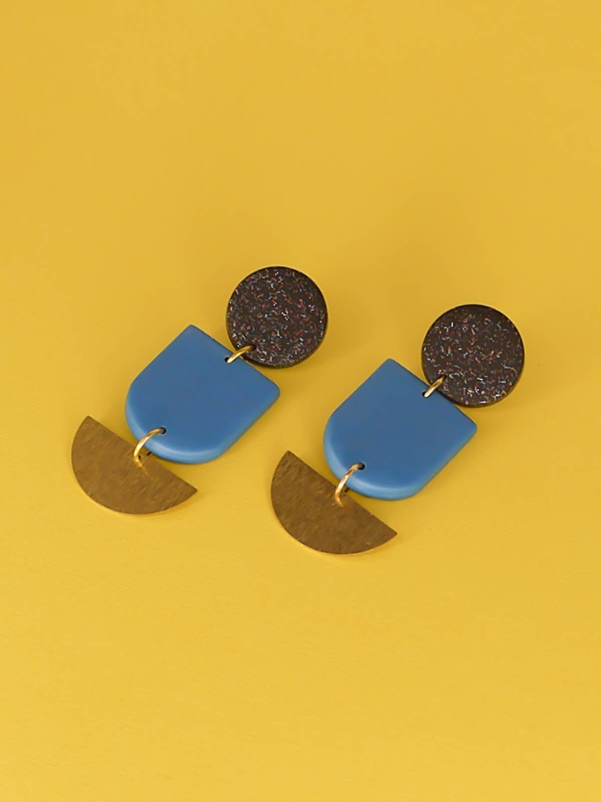 Geometric polymer clay dangle earrings with a black glitter circle stud, connected to a blue arch & a textured brass semi circle 