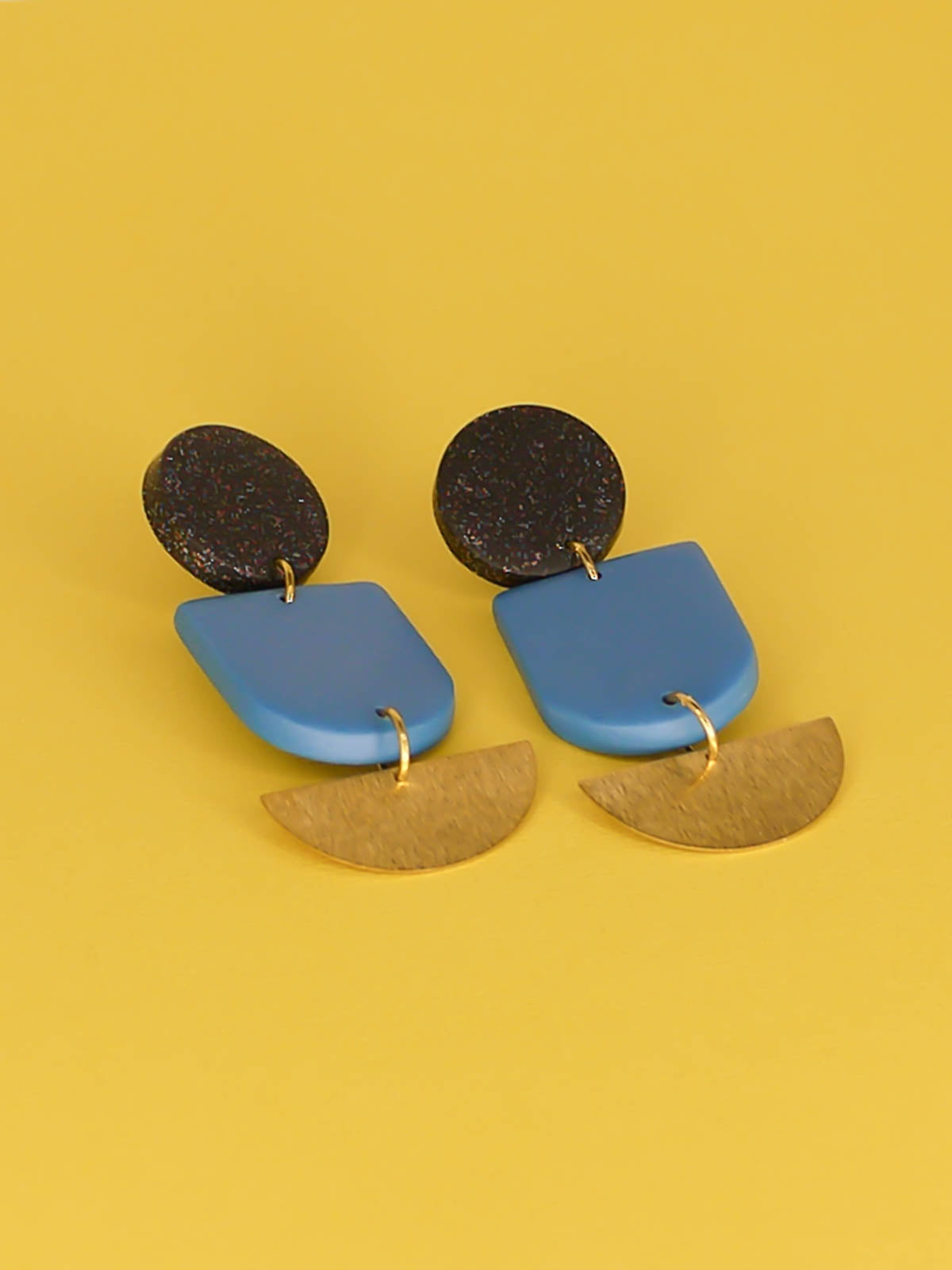 Geometric polymer clay dangle earrings with a black glitter circle stud, connected to a blue arch & a textured brass semi circle