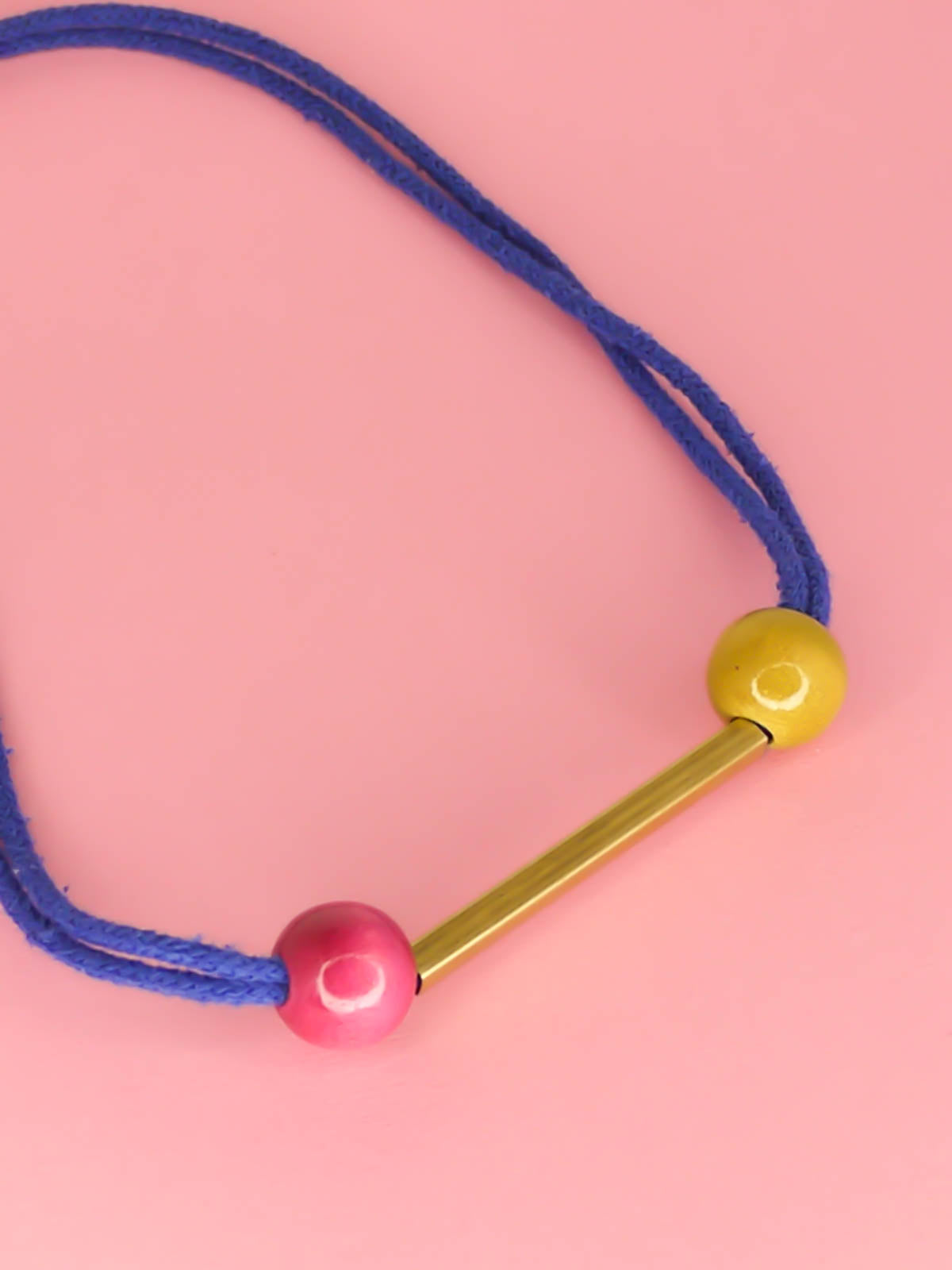 Cobalt blue rope bar necklace with a brass bar with contrasting wooden beads in pink and green with a brass clasp closure